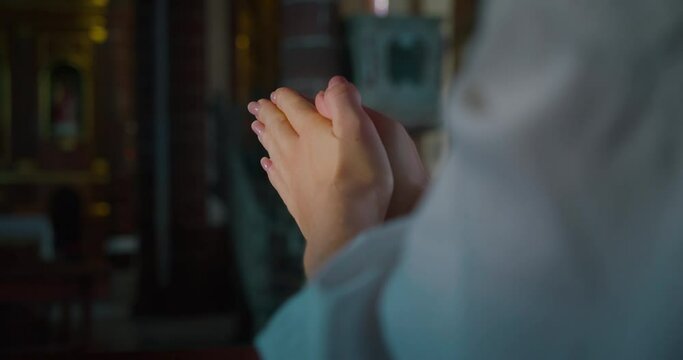 Christian woman folded hands in prayer inside a church. Religious faith in power of Christ the Redeemer and Gods love.