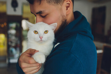 young man holding a white cat close-up.