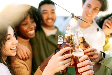 group of young people toasting with glass beer bottles at sunset on penthouse terrace. Having fun