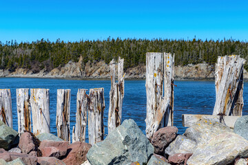 Battered and broken wooden wall holds a rock breakwater. Water behind, and trees further behind.
