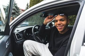 Young man sitting in a driver seat with an open car door and smiling to the camera. High quality photo