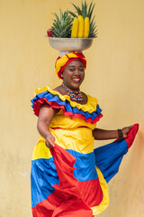 Cheerful fresh fruit street vendor aka Palenquera dancing in the Old Town of Cartagena, Colombia. Happy Afro-Colombian woman in traditional clothing, Colombian culture and lifestyle.	 - obrazy, fototapety, plakaty