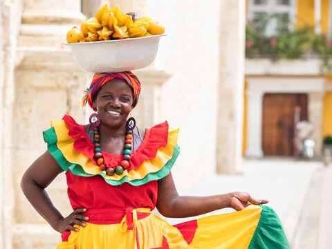 Smiling fresh fruit street vendor aka Palenquera in the Old Town of Cartagena de Indias, Colombia. Happy Afro-Colombian woman in traditional clothing, Colombian culture and lifestyle.	