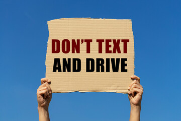 Don't text and drive text on box paper held by 2 hands with isolated blue sky background. This message board can be used as business concept about safety driving.