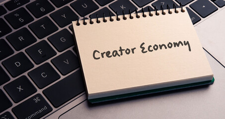 There is note book with the word Creator Economy on a laptop. It is an eye-catching image.