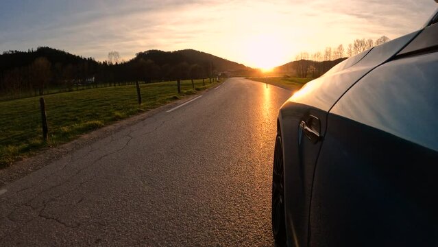 CLOSE UP: Shiny blue car driving along the curvy countryside road at golden autumn sunset. Low closeup angle of a sportscar driving fast through the curves of a country road at beautiful sunrise.