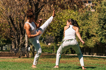 mujeres practicando patadas, ejercicios y capoeira en la ciudad con su ropa de capoeira en un...