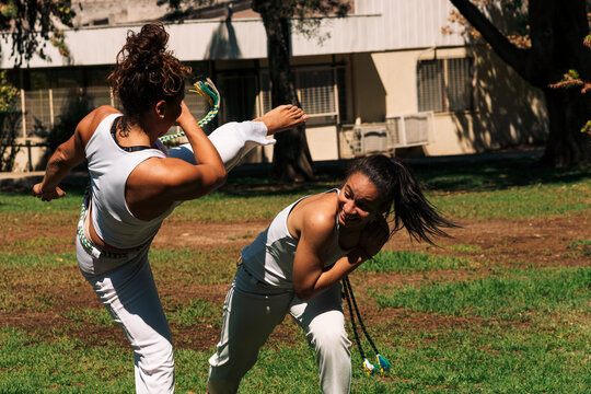 mujeres practicando patadas, ejercicios y capoeira en la ciudad con su ropa de capoeira en un parque verde en un día soleado.
