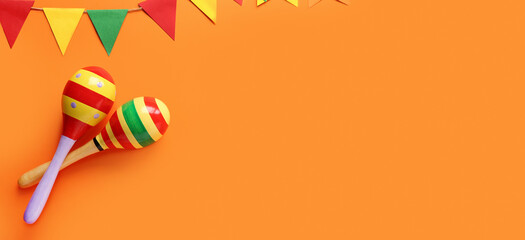 Maracas and Mexican garland on orange background with space for text