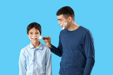 Man and his little son applying shaving foam onto faces against blue background