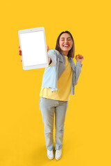 Happy young woman with big tablet computer on yellow background