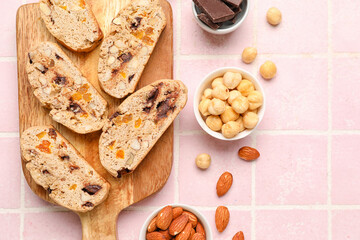 Composition with wooden board with tasty biscotti cookies, nuts and chocolate on color tile background, closeup