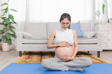 pregnant Asian people sitting on yoga mat, she use her hand touch on her abdomen, she feeling love and care her daughter, pregnancy health care promotion