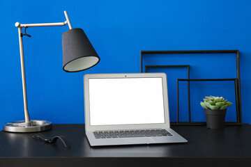 Workplace with laptop, lamp and flowerpot near blue wall