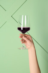 Female hand holding glass of red wine on green background