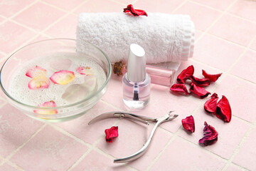 Bottles of cuticle oil, towel, nail cutter and flower petals on color tile background