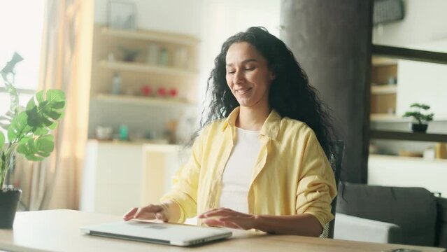 Beautiful inspired young hispanic woman stretches before productive working day at the laptop computer at home office Smiling curly freelancer enjoying great day with distance remote work indoors
