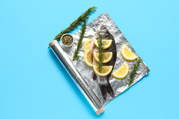 Aluminium foil roll with fresh raw fish, lemon slices, rosemary and spices on color background