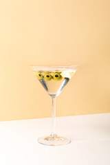 Glass of martini with olives on beige background