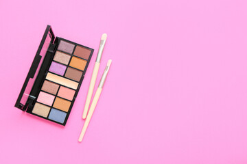 Palette of eyeshadows with brushes on pink background