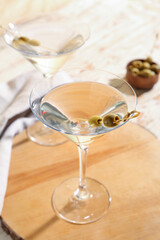 Glasses of tasty martini and olives on light wooden table