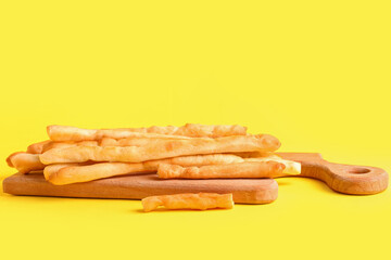 Wooden board with tasty Italian Grissini on yellow background