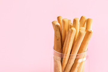Jar with tasty Italian Grissini on pink background, closeup