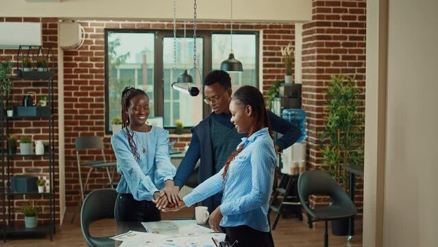 Cheerful colleagues celebrating success, uniting hands and cheering after obtaining business profit. Happy office workers feeling pleased about development results, successful teamwork.