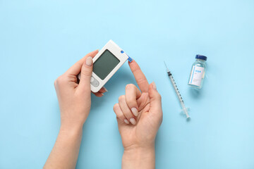 Woman using glucometer on blue background. Diabetes concept