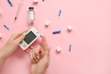 Woman using glucometer on pink background. Diabetes concept