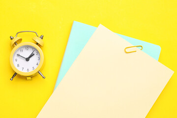 Paper sheets and clock on yellow background