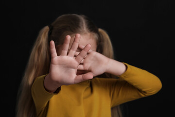 Girl making stop gesture against black background, focus on hands. Children's bullying