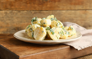 Plate of tasty Potato Salad with greens on wooden background