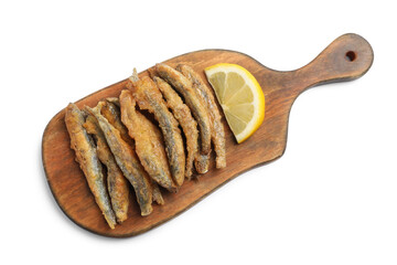 Wooden board with delicious fried anchovies and lemon on white background, top view