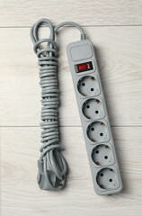 Power strip with extension cord on white wooden floor, top view. Electrician's equipment