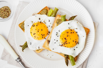 Delicious sandwiches with fried eggs and asparagus on light background