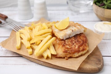 Tasty soda water battered fish, potato chips and lemon slice on white wooden table