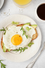 Delicious sandwich with fried egg, arugula and avocado on light background