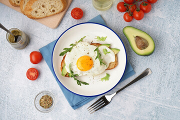 Delicious sandwich with fried egg, avocado and arugula on light background