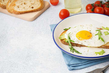 Delicious sandwich with fried egg, avocado and arugula on light background