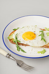Delicious sandwich with fried egg, avocado and arugula on grey background