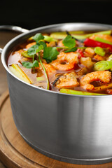Saucepan with delicious Tom Yum soup on wooden board, closeup