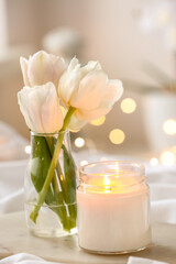 Burning candle and vase with tulips on bed, closeup