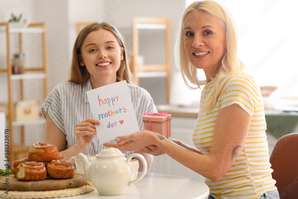 Canvas Prints Young woman greeting her mother with card and gift in kitchen