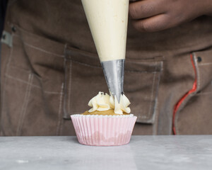 Piping buttercream on a vanilla cupcake, decorating cupcakes, hand piping tall frosting on...