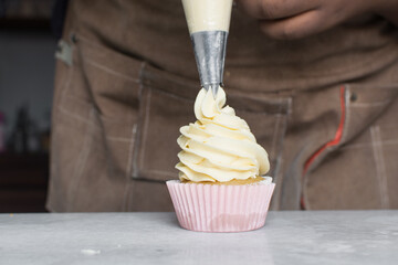 Piping buttercream on a vanilla cupcake, decorating cupcakes, hand piping tall frosting on...