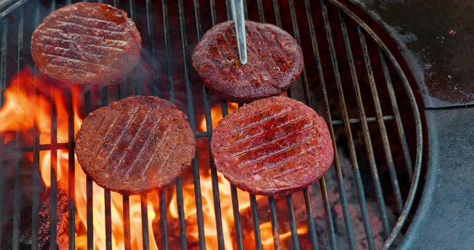 Top down rotating shot of person flipping vegan burgers cooking over fiery outdoor barbeque pit