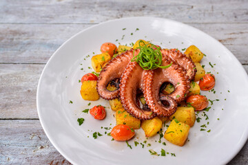Octopus with potatoes and cherry tomatoes on white wooden table. Brazilian gastronomy.