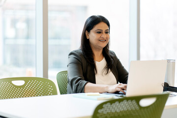 Confident smiling Indian businesswoman using laptop computer, typing on keyboard, working online in...