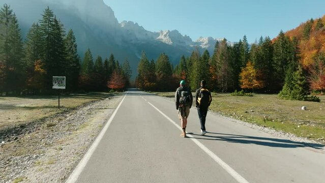 Aerial passes 2 younng guys walking in the middle of an empty road in Valbona Valley, Albania